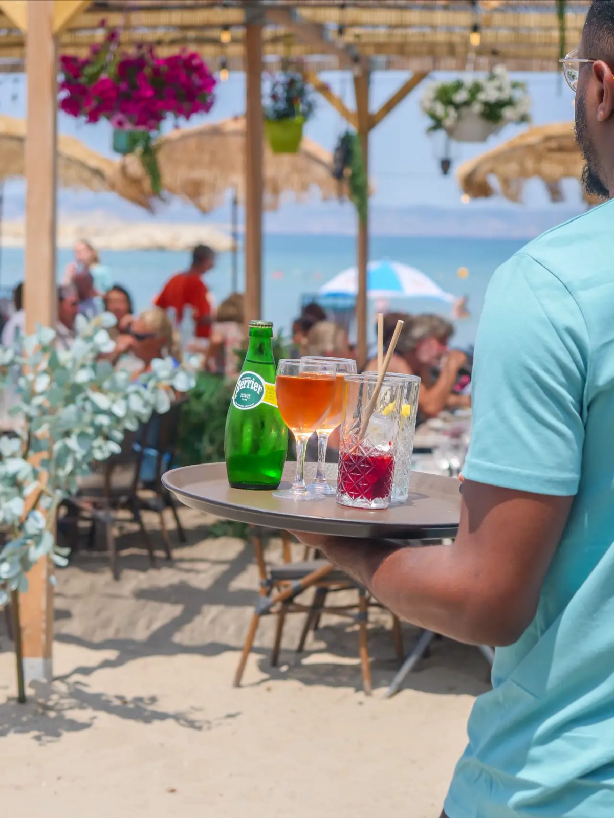 Serveur portant un plateau de cocktails et Perrier face à la mer