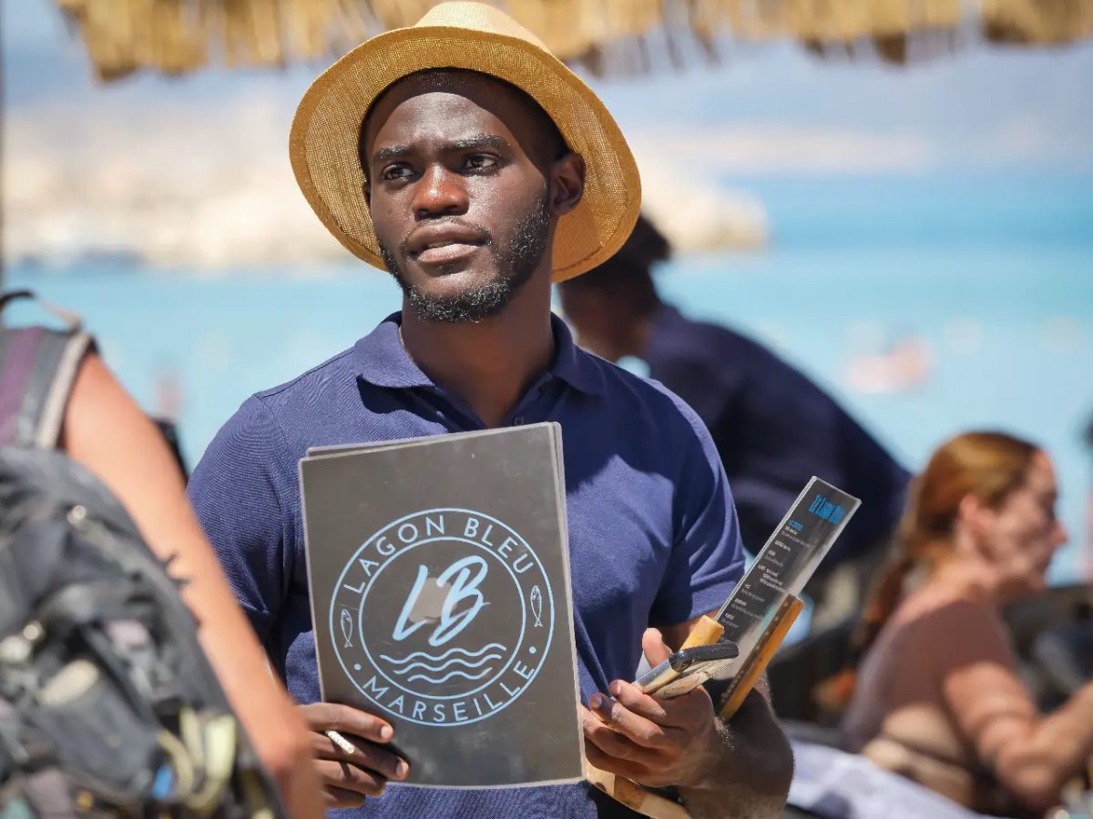 Serveur en polo bleu et chapeau présentant les menus du Lagon Bleu