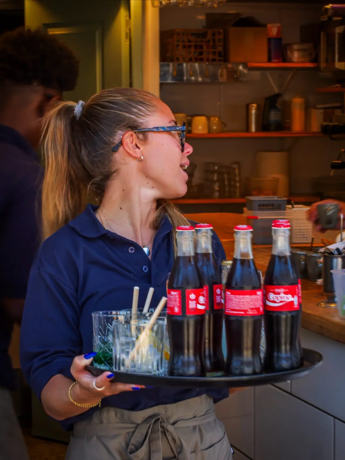 Serveuse souriante portant un plateau de bouteilles en cuisine