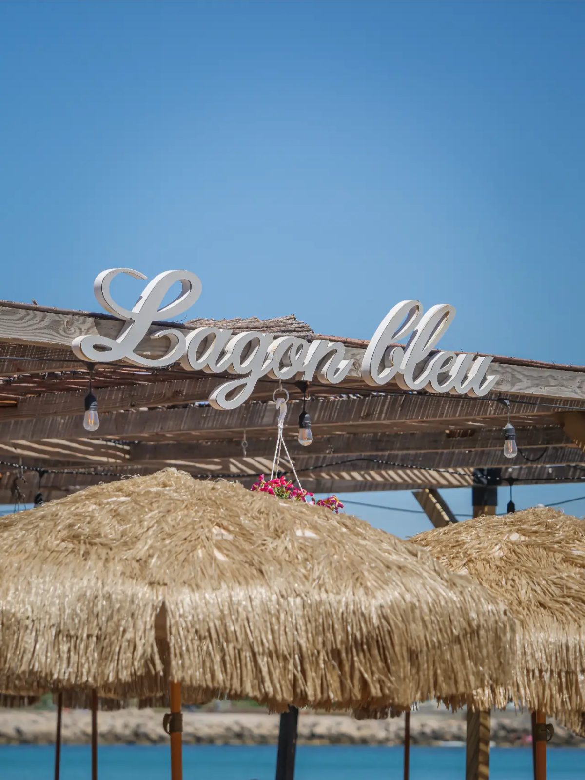 Enseigne cursive Lagon bleu sous ciel bleu, parasols en premier plan