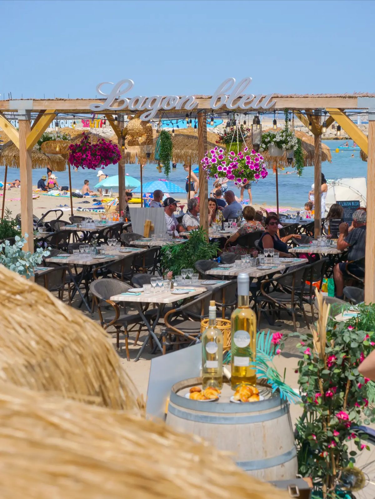 Terrasse pleine avec bouteilles de vin face à la plage